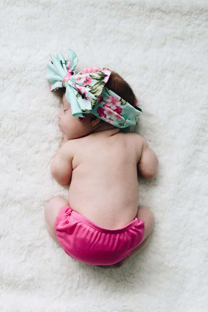 Slika novorojenčka na mehki podlagi z veliko pisano pentljo na glavi. 