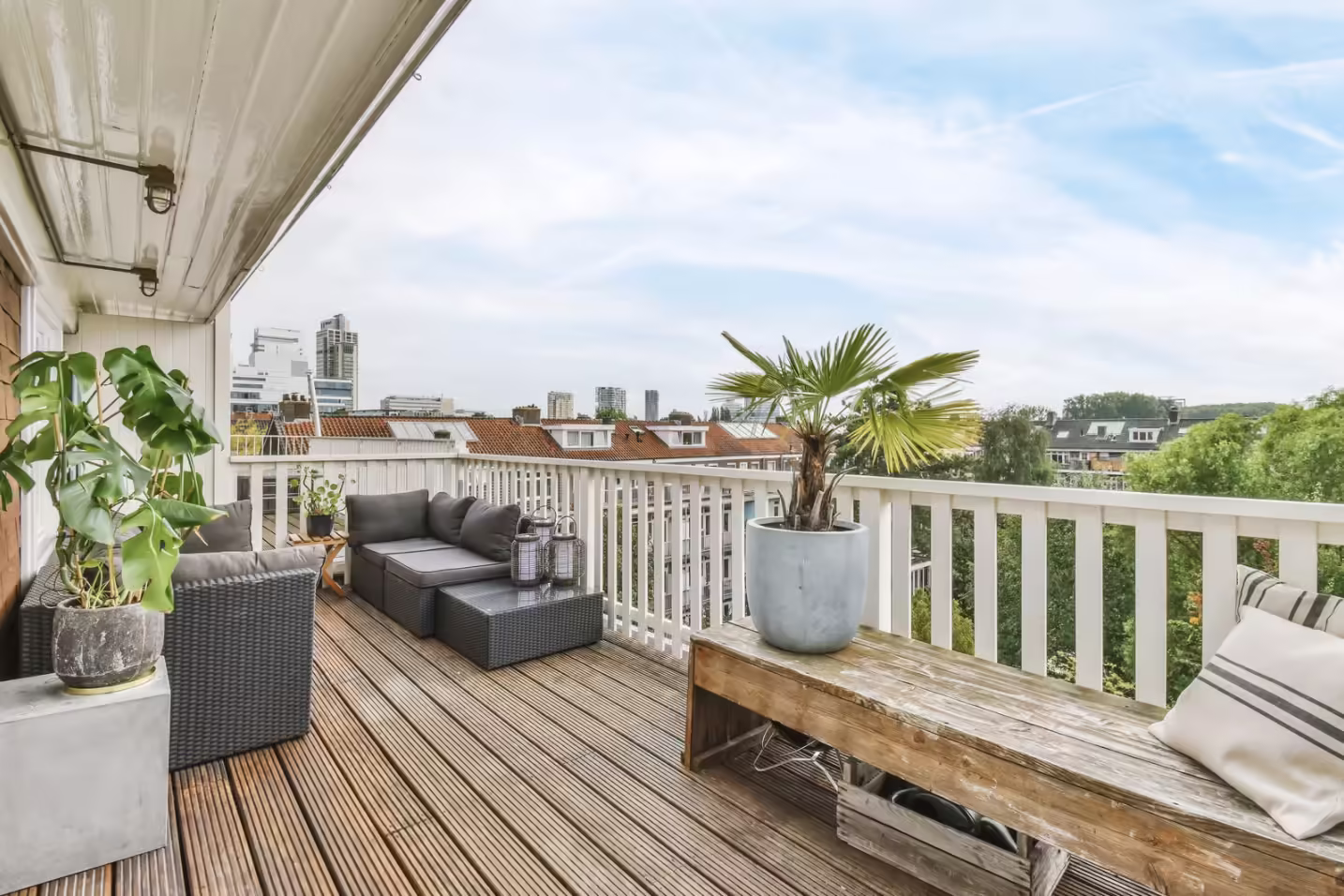 Prenovljen balkon z lesenim podom, belimi ograjami, udobnim vrtnim pohištvom in okrasnimi rastlinami po sanaciji balkona.